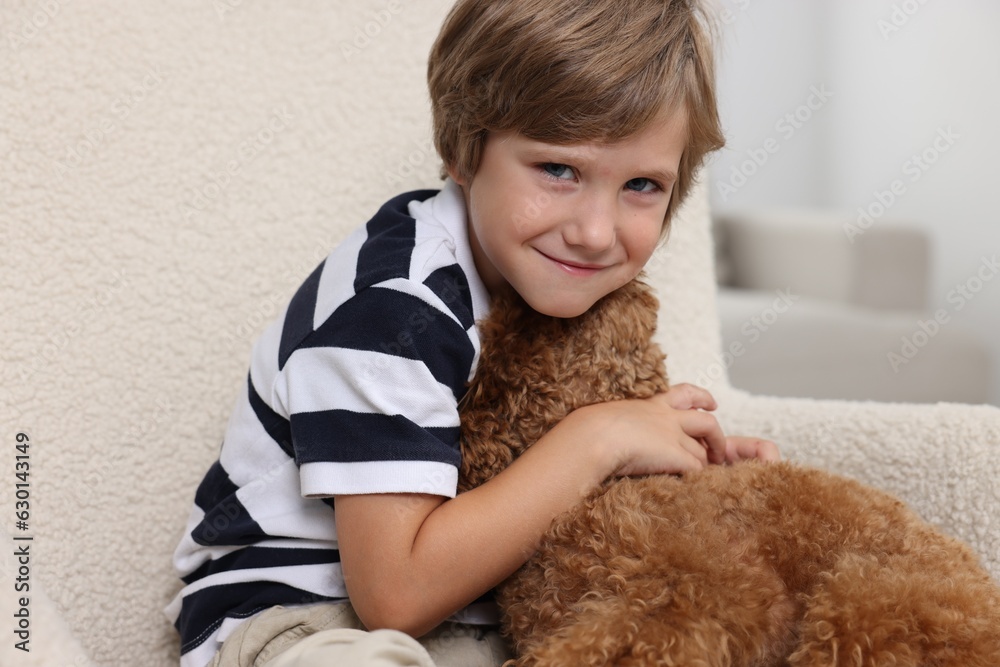 Little child with cute puppy in armchair indoors. Lovely pet