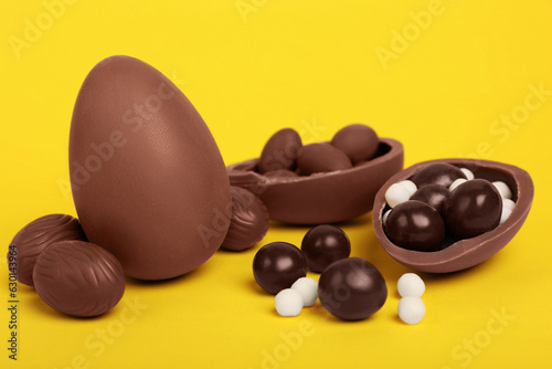 Delicious chocolate eggs and candies on yellow background, closeup
