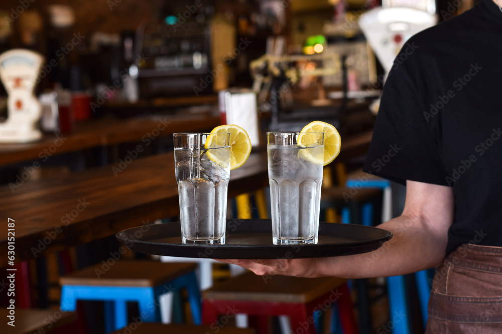 Restaurant server holding a tray with two glasses with water and lemon slice