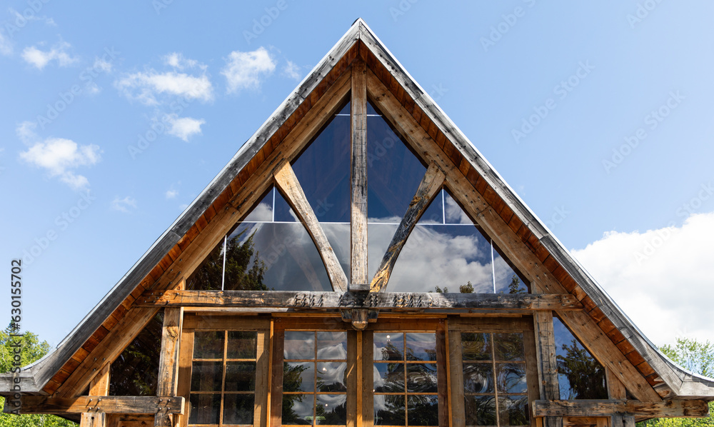 Obraz premium vue sur le haut d'une maison en bois avec la façade en verre lors d'une journée ensoleillée avec la réflection du ciel dans la vitre