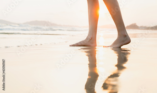 Woman's legs stand on the beach at sunset time.