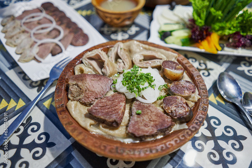 traditional Kazakh Asian dish Beshbarmak: noodles with lamb and onions close-up on a plate on the table. near the broth in bowls. dastarkhan. bolied beef and horse meat photo