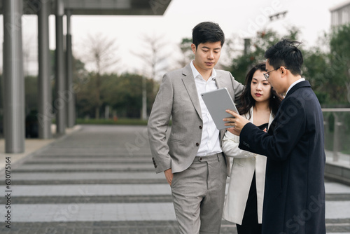 Asian business people using tablet computer and talking outdoors.