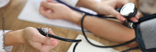 Close up of doctor using sphygmomanometer with stethoscope checks blood pressure of patient in hospital.