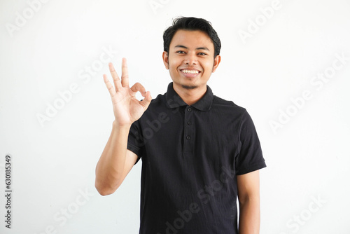 young Asian man smiling friendly while giving OK finger sign wearing black polo t shirt isolated on white background