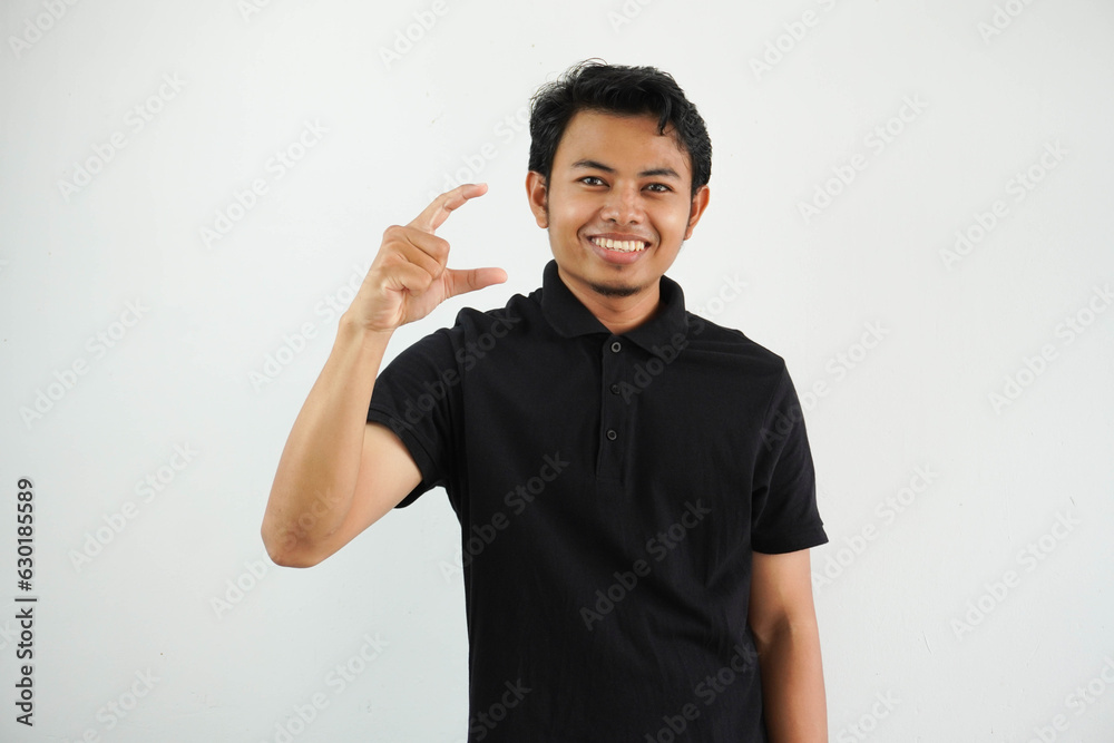 young asian man posing on a white backdrop holding something little with forefingers, smiling and confident, wearing black polo t shirt. young asian man posing on a white backdrop holding something little with forefingers, smiling and confident, wearing black polo t shirt.