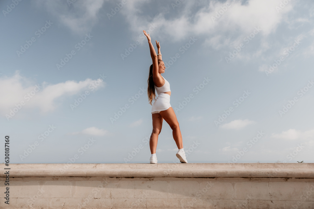 Obraz premium Fitness woman sea. Active, happy middle-aged woman in white sportswear exercises outdoors in a park over sea. Healthy lifestyle, physical activity and female fitness pilates and yoga routines.