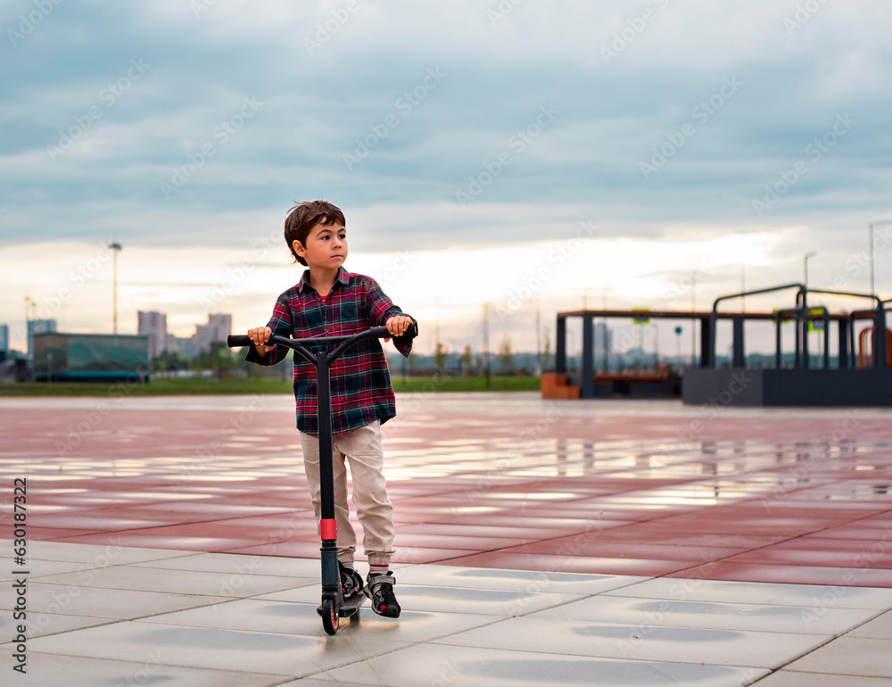 Obraz premium Little boy riding a scooter at the stadium in the evening.