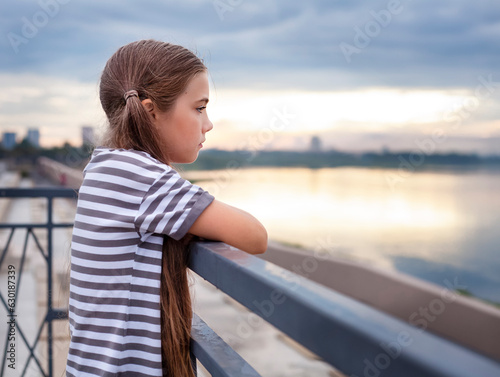 Cute little girl in striped t-shirt standing on the bridge and looking away © Алена Ягупа
