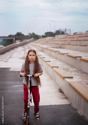 Little girl riding a scooter on the embankment of the river