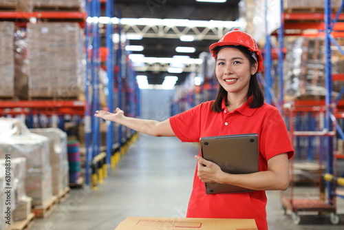 Portrait of warehouse workers young asian woman standing and using computer while posing show something on hand and controlling stock and inventory in retail warehouse logistics, distribution center