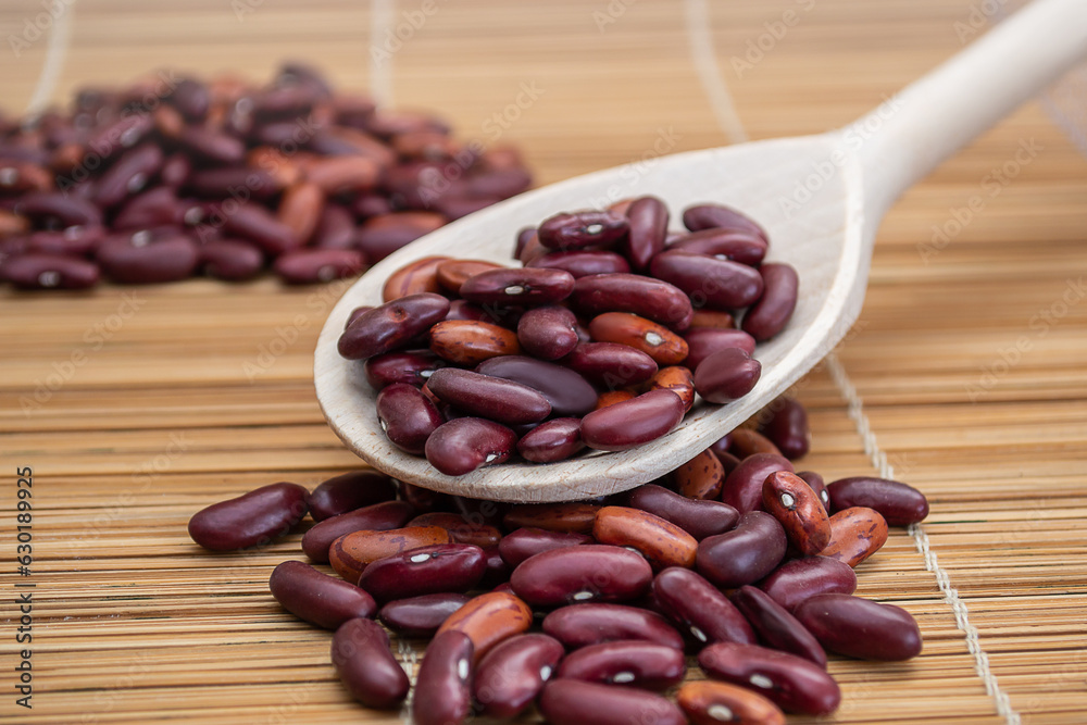 A wooden spoon filled with red beans on top of a bamboo mat A wooden spoon filled with red beans on top of a bamboo mat