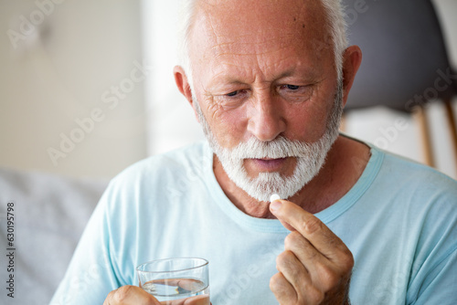 Senior man takes pill with glass of water in hand. Stressed mature man drinking sedated antidepressant meds. Man feels depressed, taking drugs. Medicines at work