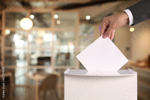 Man putting his vote into ballot box on blurred background, closeup