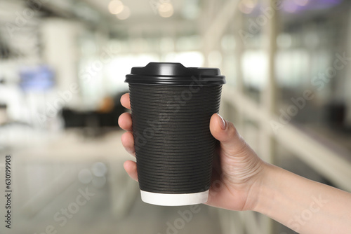 Coffee to go. Woman holding paper cup of hot drink on blurred background, closeup