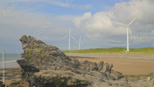 Wind turbines on beach on cloudy summer day with foreground rock formation. Half speed slow motion. photo