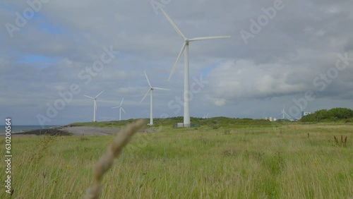 Windmills rotating through yellowed grasses with rise up clearing grass showing cloudy summer sky. Half speed slow motion. photo