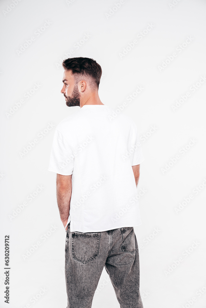 Fototapeta premium Portrait of handsome smiling stylish hipster lambersexual model. Sexy man dressed in white T-shirt and jeans. Fashion male isolated on white background in studio. Back view. Mockup