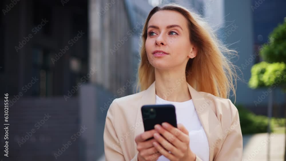 Beautiful happy blond businesswoman in a formal suit types on her mobile phone outdoors. Girl confidently uses a new social network app against the backdrop of the bustling downtown. Business people. Beautiful happy blond businesswoman in a formal suit types on her mobile phone outdoors. Girl confidently uses a new social network app against the backdrop of the bustling downtown. Business people.