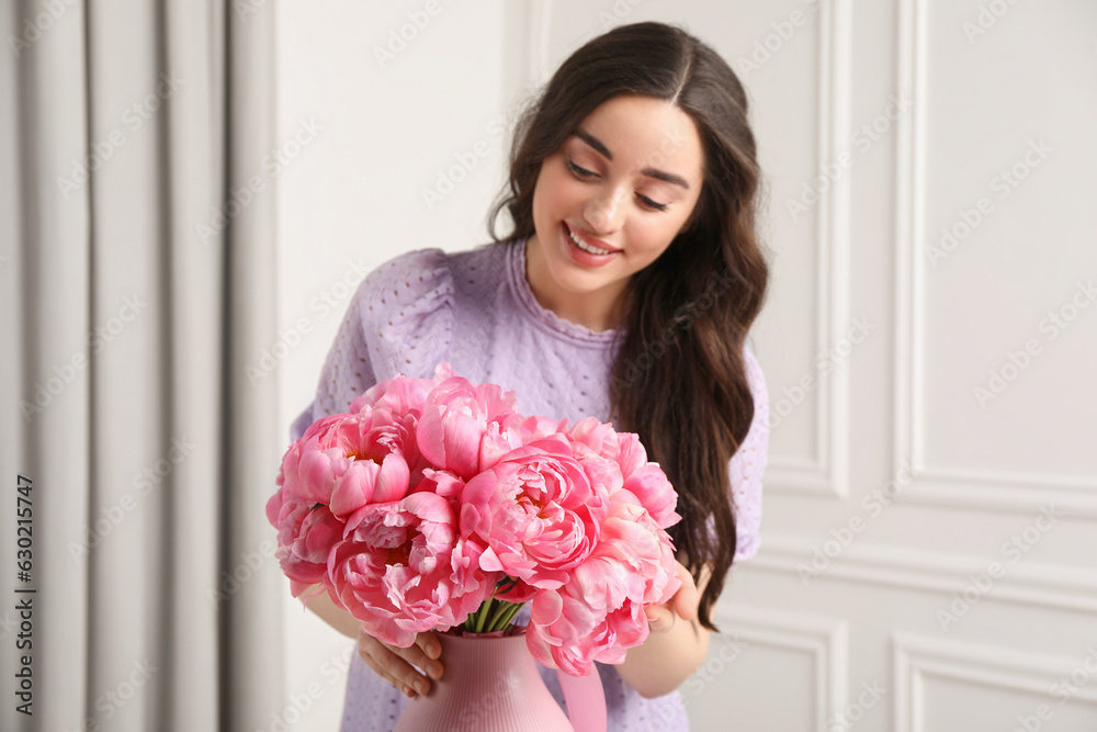 Beautiful young woman with bouquet of pink peonies in vase indoors, selective focus Beautiful young woman with bouquet of pink peonies in vase indoors, selective focus