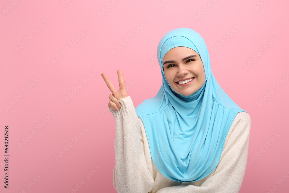 Muslim woman in hijab showing V-sign on pink background, space for text Muslim woman in hijab showing V-sign on pink background, space for text
