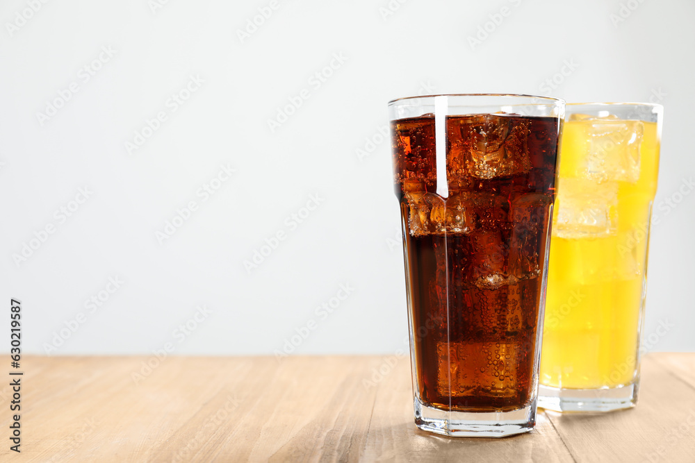 Glasses of different refreshing soda water with ice cubes on wooden table, space for text Glasses of different refreshing soda water with ice cubes on wooden table, space for text