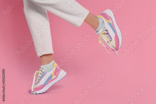 Woman wearing pair of new stylish sneakers on pink background, closeup