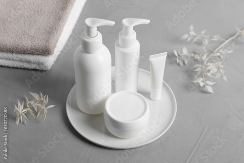 Different cosmetic products, towels and dry leaves on grey table