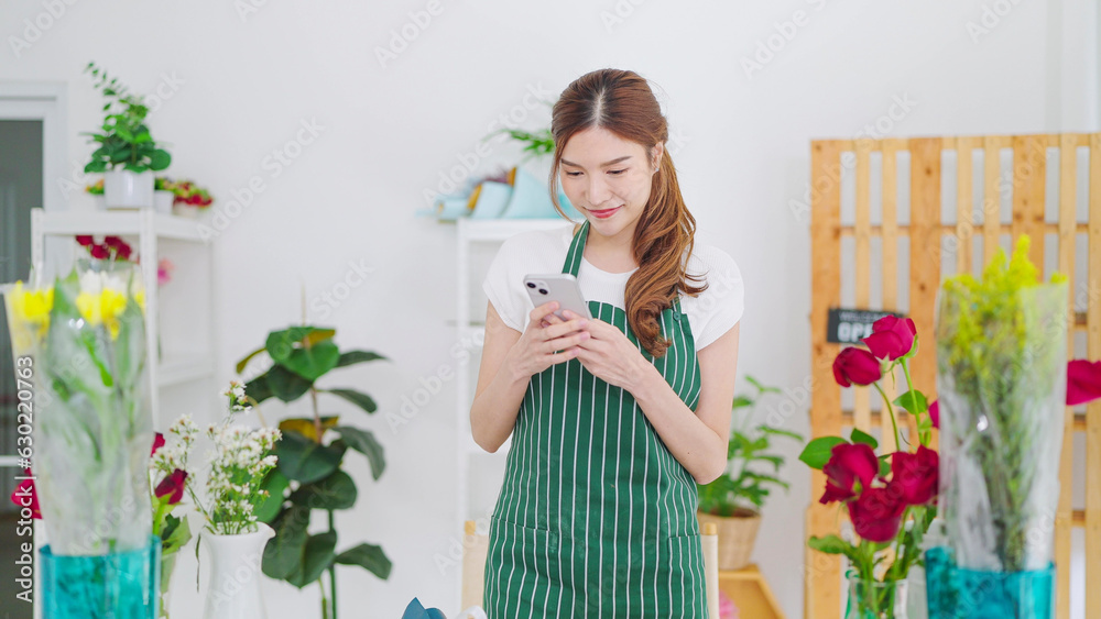 Beautiful young asian women owner floral store in apron typing on smartphone taking order with client or post on social media. Small business concept Beautiful young asian women owner floral store in apron typing on smartphone taking order with client or post on social media. Small business concept