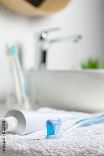 Plastic toothbrush with paste and tube on white towel in bathroom  closeup. Space for text