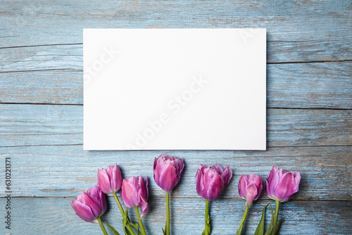 Blank white canvas mockup with flowers on blue wood background. Artistic canvas hanging, mockup design