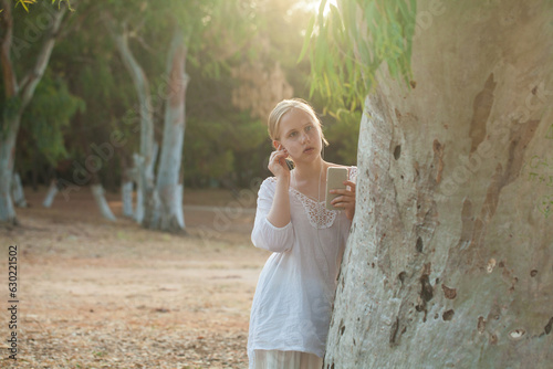 Teenage girl in white shirt lisening to music in headphones on the background of forest photo