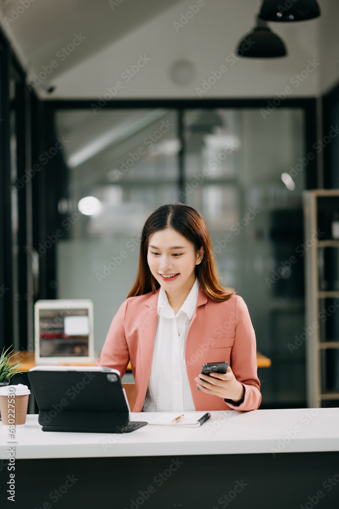 Young beautiful Asian woman typing on tablet and laptop while sitting at the working white table modern office Young beautiful Asian woman typing on tablet and laptop while sitting at the working white table modern office