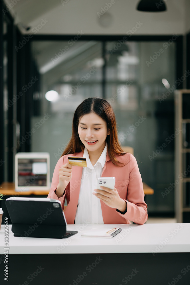 Asian Woman using smart phone for mobile payments online shopping,omni channel,sitting on table,virtual icons graphics interface screen Asian Woman using smart phone for mobile payments online shopping,omni channel,sitting on table,virtual icons graphics interface screen
