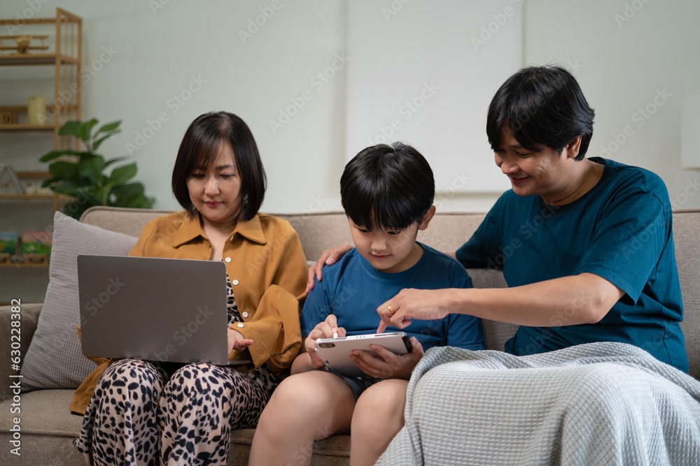 Happy parents with two kids using smartphone at home together, sitting on couch, smiling mother and father with little son looking at phone screen, having fun Happy parents with two kids using smartphone at home together, sitting on couch, smiling mother and father with little son looking at phone screen, having fun
