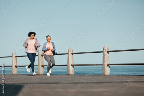 Senior, fitness and women friends at the beach for running, bond and morning cardio in nature together. Ocean, workout and elderly female runners happy, talking and enjoy fresh air, run and training