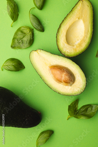 Close up of two halves of avocado and basil leaves and copy space on green background