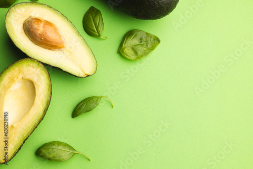 Close up of two halves of avocado and basil leaves and copy space on green background