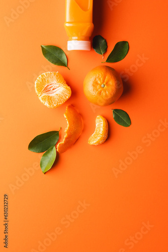 Close up of bottle with juice, tangerine, segments and leaves with copy space on orange background