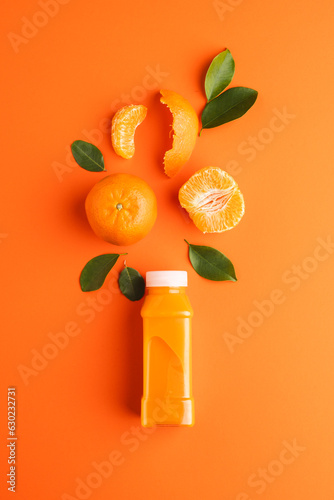 Close up of bottle with juice, tangerine, segments and leaves with copy space on orange background