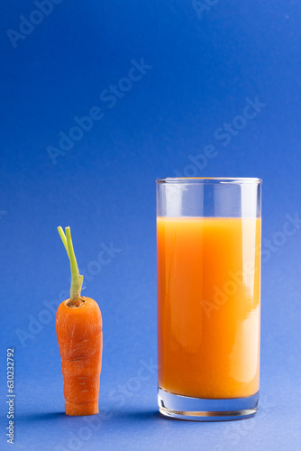 Close up of carrot and glass of carrot juice with copy space on blue background