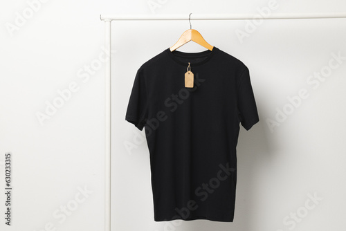 Black t shirt with tag hanging from clothes rack with copy space on white background