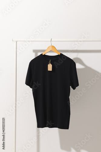 Black t shirt with tag hanging from clothes rack with copy space on white background