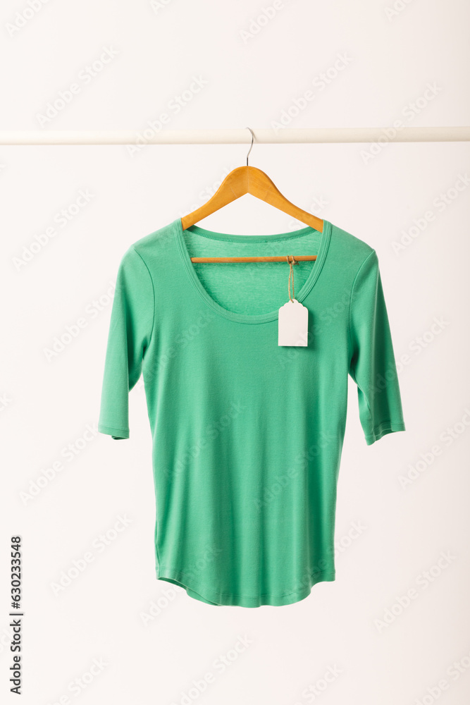 Naklejka premium Green t shirt with tag on hanger hanging from clothes rail with copy space on white background
