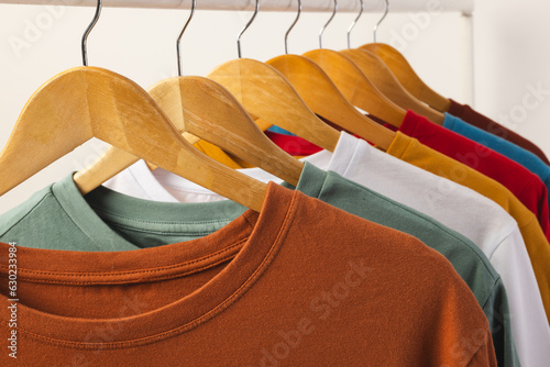 Multi coloured t shirts on hangers hanging from clothes rail and copy space on white background