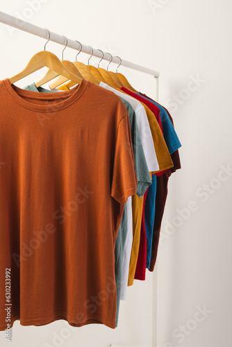 Multi coloured t shirts on hangers hanging from clothes rail and copy space on white background