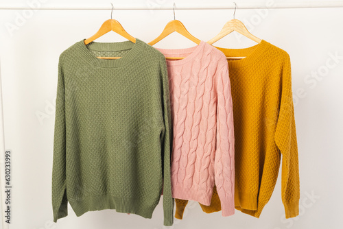 Three sweaters hanging from clothes rail with copy space on white background