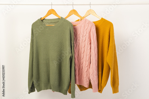 Three sweaters hanging from clothes rail with copy space on white background