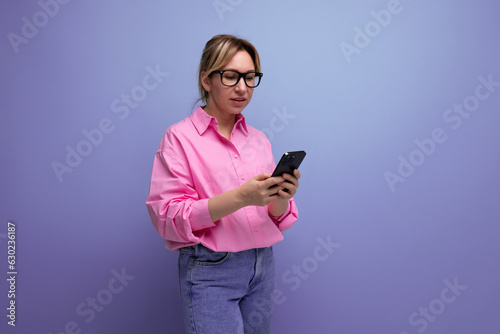 young caucasian blond leader careerist woman with ponytail with glasses dressed in a pink blouse uses a smartphone