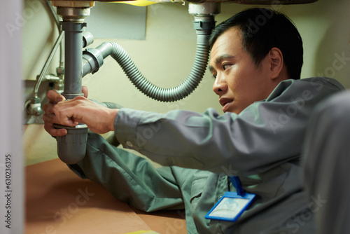 Plumber cleaning clogged pipe under kitchen sink